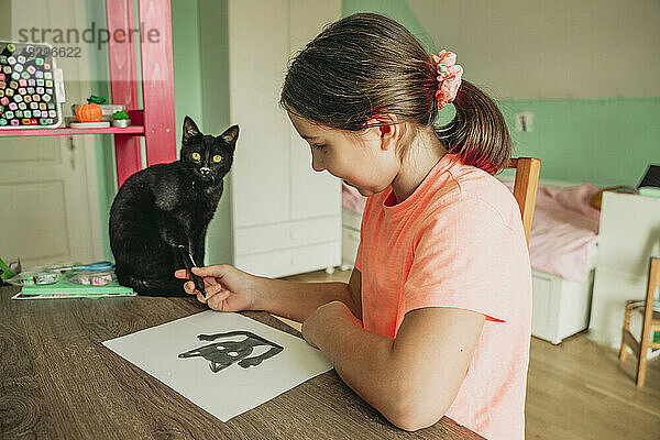 Mädchen gibt der Katze  die zu Hause auf dem Tisch sitzt  einen Filzstift