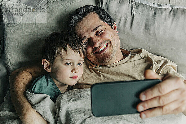 Vater und Sohn machen Selfie mit Smartphone im Bett