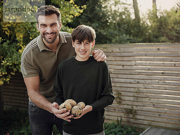 Vater und Sohn stehen im Garten und halten frisch geerntete Kartoffeln in der Hand