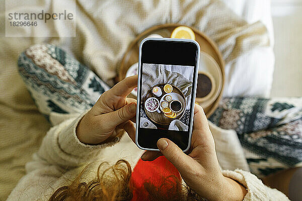 Frau fotografiert Essen mit Smartphone zu Hause im Bett