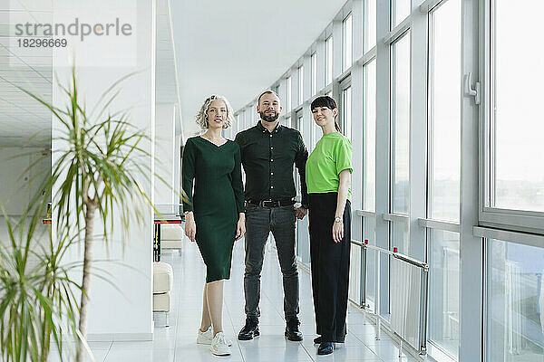 Drei Geschäftsleute in grüner Kleidung stehen auf der Büroetage