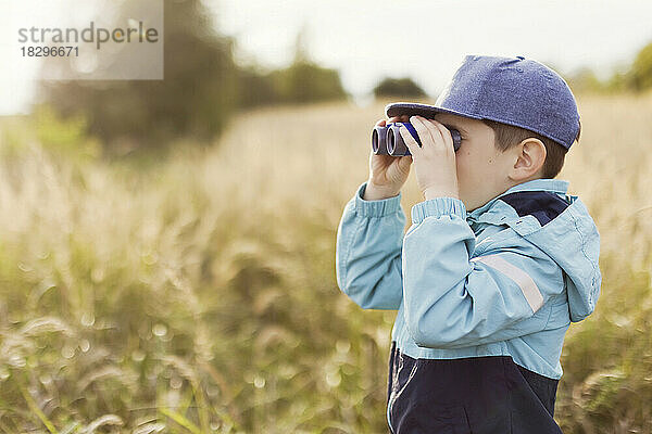 Junge schaut durch ein Fernglas auf dem Feld