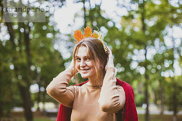 Lächelnde Frau hält Ahornblätter auf dem Kopf im Park