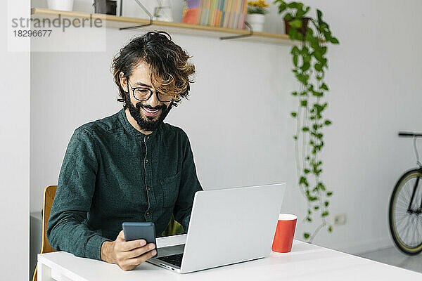 Lächelnder Geschäftsmann  der sein Mobiltelefon am Schreibtisch benutzt