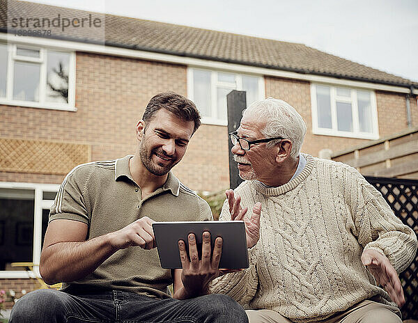 Vater und Sohn sitzen im Garten und nutzen ein digitales Tablet