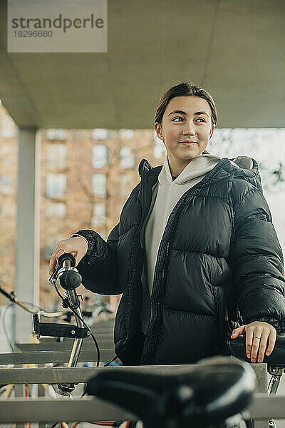 Lächelndes Teenager-Mädchen in schwarzer Jacke steht am Fahrradparkplatz