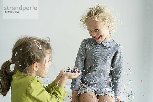 Happy girl with friend having fun with confetti at home