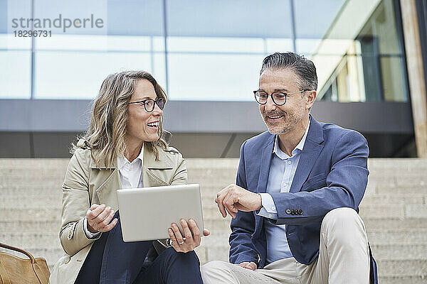 Lächelnde Geschäftsfrau hält Tablet-PC in der Hand und diskutiert mit Kollegen über Schritte