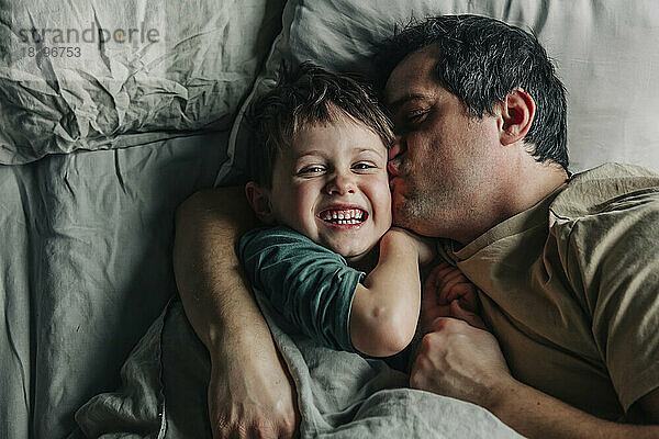 Man kissing son lying on bed in bedroom