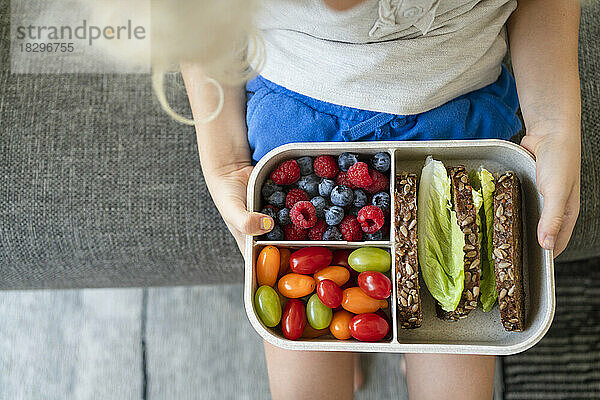 Hands of girl holding lunch box with healthy food on sofa at home