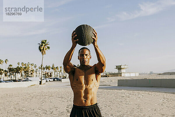 Aktiver Mann hält Ball und trainiert am Strand