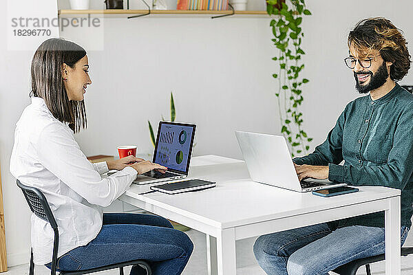Lächelnde Freiberufler nutzen Laptops am Schreibtisch im Büro