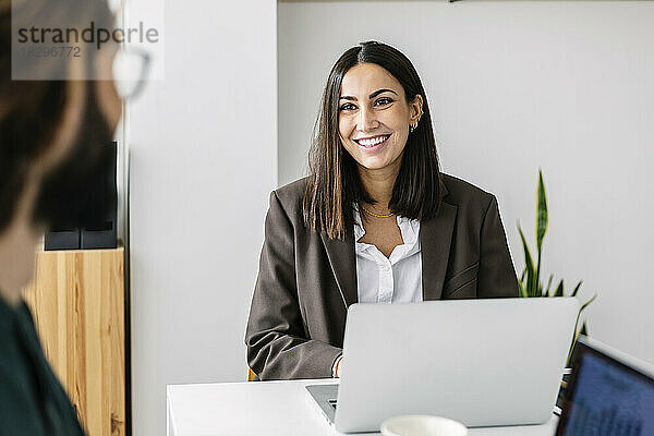 Glückliche Geschäftsfrau mit Laptop und Blick auf Kollegen im Büro