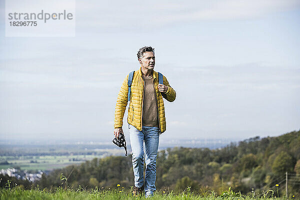 Reifer Mann mit Rucksack und Fernglas beim Wandern im Urlaub