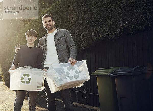 Father and son standing outdoors carrying recycling boxes with separated waste