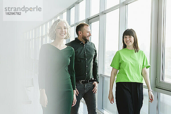 Drei glückliche Geschäftsleute in grüner Kleidung gehen durch die Büroetage