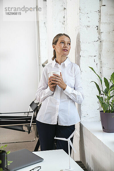 Nachdenkliche reife Geschäftsfrau mit Kaffeetasse lehnt an der Wand