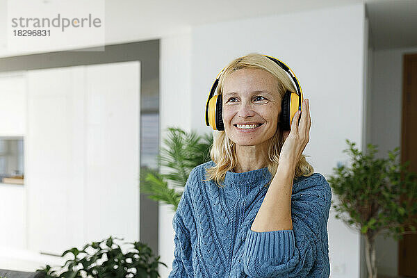 Happy woman wearing wireless headphones listening music at home