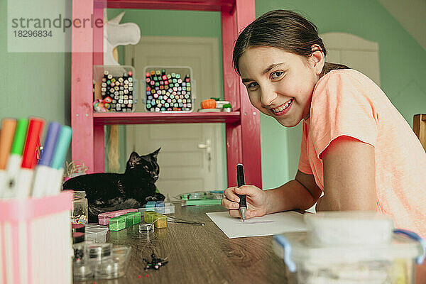 Glückliches Mädchen zeichnet ein Bild auf Papier von einer Katze auf dem Tisch