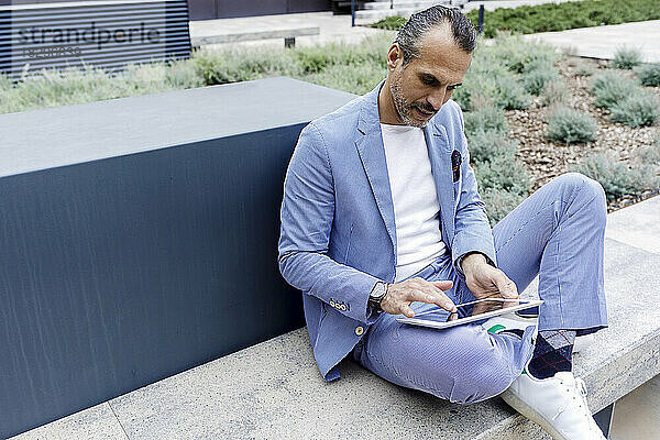 Geschäftsmann benutzt Tablet-Computer auf Bank sitzend