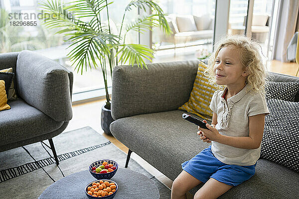 Smiling girl holding remote control on sofa in living room
