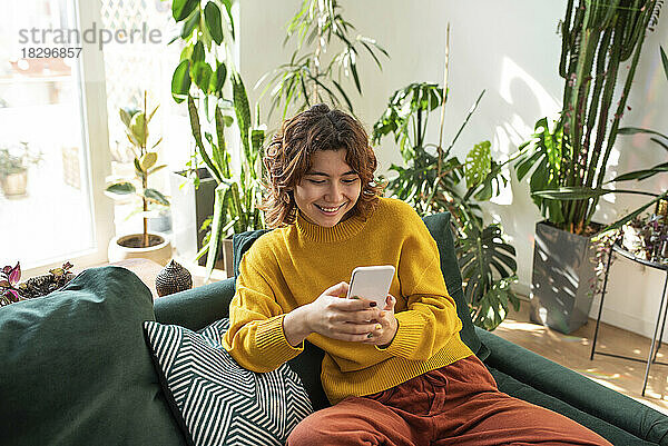 Lächelnde junge Frau mit Smartphone auf der Couch sitzend