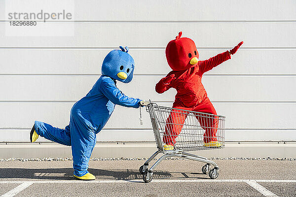 Freunde in roten und blauen Entenkostümen amüsieren sich mit einem Einkaufswagen an der Wand