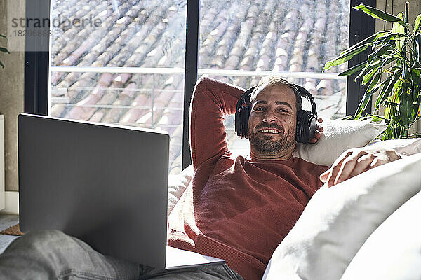Glücklicher Mann mit Kopfhörern  der zu Hause mit Laptop sitzt