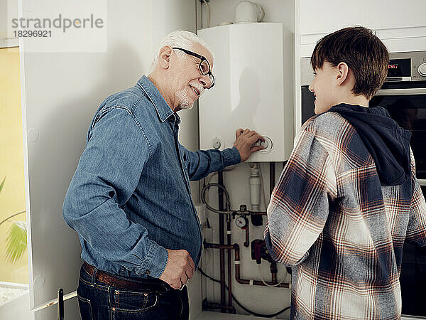 Lächelnder Enkel und Großvater prüfen den Heizkessel zu Hause auf Energieeinsparung