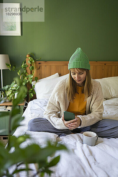 Frau mit Strickmütze sitzt zu Hause im Bett