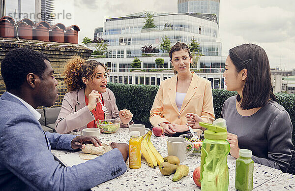 Geschäftsfrau isst zu Mittag und unterhält sich mit Kollegen  die am Tisch sitzen