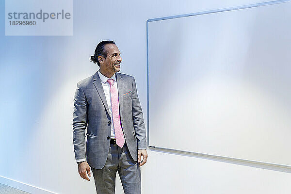 Glücklicher Geschäftsmann blickt im Konferenzraum auf das Whiteboard