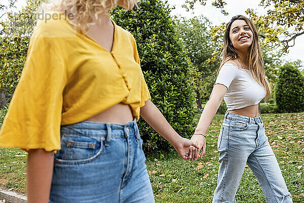Lächelnde Frau hält die Hand eines Freundes und geht im Park spazieren
