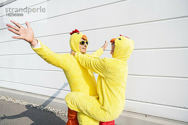 Sorglose Freunde in Hühnerkostümen stehen an einem sonnigen Tag vor der Wand