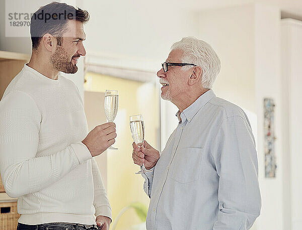 Älterer Mann und erwachsener Sohn feiern zu Hause und stoßen mit Champagner an