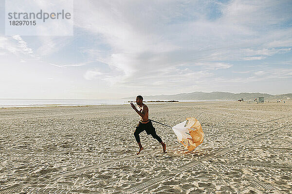 Mann läuft mit Fallschirm am Strand