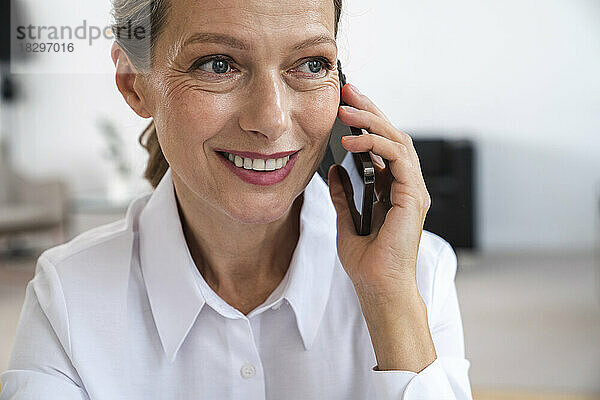 Glückliche reife Geschäftsfrau  die im Büro über ihr Smartphone spricht