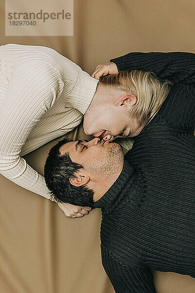 Couple kissing lying on brown backdrop