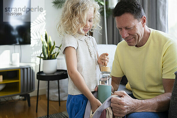 Lächelnder Vater und Tochter packen Wasserflasche in Rucksack