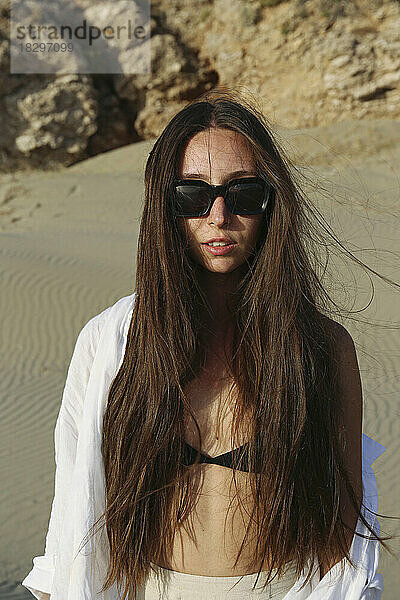 Junge Frau mit Sonnenbrille steht am Strand