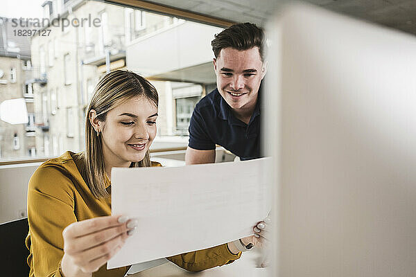 Lächelnde junge Geschäftsfrau liest Dokument mit Kollegen im Büro