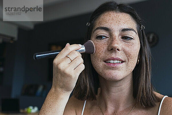 Frau mit Sommersprossengesicht  die zu Hause Make-up aufträgt