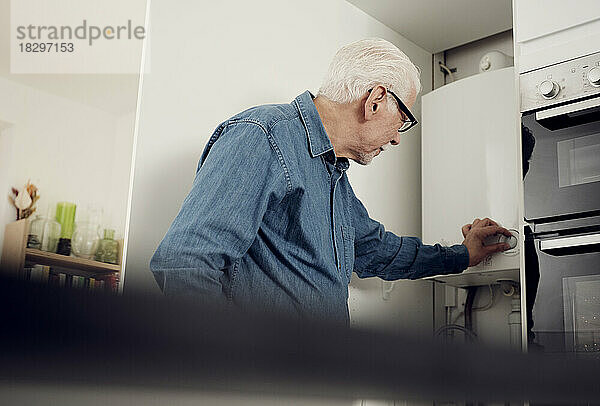 Älterer Mann passt Heizkessel an  um zu Hause Energie zu sparen