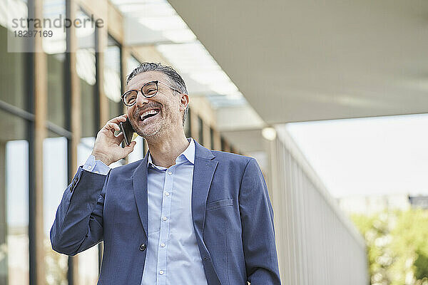 Glücklicher Geschäftsmann  der vor dem Gebäude mit dem Smartphone spricht