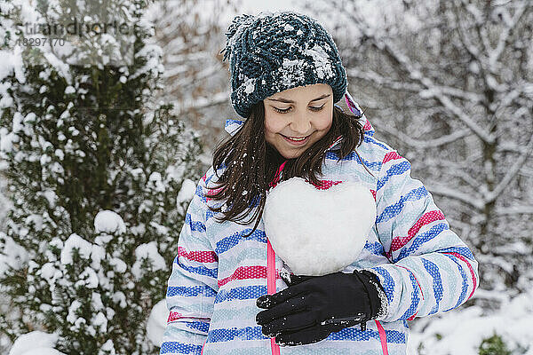 Lächelndes Mädchen  das im Winter einen herzförmigen Schneeball hält