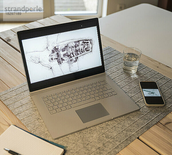 Zeichnung einer Windkraftanlage auf dem Laptop-Bildschirm  gehalten per Smartphone am Schreibtisch