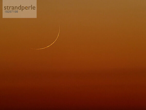 View of crescent moon rising against reddish sky at dusk