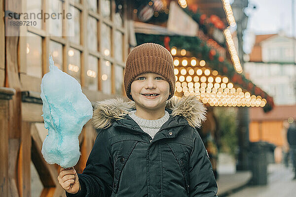Fröhlicher Junge mit Zuckerwatte steht auf dem Weihnachtsmarkt