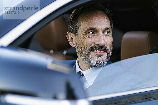Lächelnder reifer Geschäftsmann sitzt im Auto