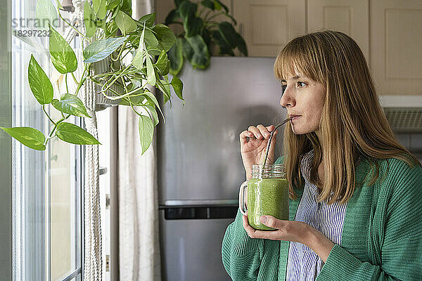 Frau trinkt zu Hause grünen Smoothie